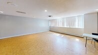 Located at 75 Charolais Blvd in Brampton, Ontario, this single-floor space offers a generously sized, open-concept layout well-suited for a variety of uses, from community gatherings to events and meetings. The main hall is the centerpiece of the space, featuring warm parquet wood flooring across the primary open area, complemented by light-toned ceramic tile in the entryway and adjoining sections. The textured ceilings are fitted with recessed pot lights throughout, providing bright, even illumination across the entire floor. A row of large windows along one wall allows natural light to fill the space, enhanced by baseboard heating units positioned beneath them. The hall is equipped with a ceiling-mounted projector and a retractable projection screen, making it functional for presentations or screenings. A compact kitchenette area is accessible toward the rear, alongside a dining area with table and chairs. Interior windows connect ancillary spaces to the main hall, offering added versatility. The layout also includes a clearly marked exit door and fire safety features. The overall ambiance is clean, bright, and practical, offering an open and adaptable environment ready to accommodate a wide range of programming or events.