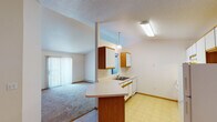 Located at 3550 42nd St S in Fargo, North Dakota, this single-floor unit offers a practical and well-organized layout suited for comfortable everyday living. The kitchen is open and functional, featuring white cabinetry with wood-tone trim, a white electric range, a full-size refrigerator, and a double-basin sink set into a peninsula with a breakfast bar overhang. A pendant light fixture adds a focal point above the dining area, which flows seamlessly into the kitchen and entry zone, both finished with easy-to-maintain tile flooring. The living room is carpeted and spacious, filled with natural light from a large sliding glass door fitted with vertical blinds that provide access to an outdoor area. Baseboard heating runs throughout the unit, ensuring consistent warmth. The bedrooms are carpeted and bright, with one featuring a walk-in closet equipped with dual wire shelving racks, and another offering a standard reach-in closet. Two full bathrooms mirror each other in design, each including a single-sink vanity with a large mirror and globe lighting, a toilet, and a tub-shower combination, all set on tile flooring. Textured ceilings are present throughout, giving the unit a consistent, cohesive finish.