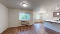 Located at 8527 NE Quatama St in Hillsboro, Oregon, this single-level unit offers a practical and well-designed layout suited for comfortable everyday living. The open-concept living and dining area is finished with warm wood-style flooring that extends throughout the main living spaces, creating a cohesive and inviting atmosphere. Multiple windows allow natural light to filter in, with views of surrounding greenery, while a wall-mounted HVAC unit provides convenient climate control. An elegant chandelier anchors the dining area, which connects seamlessly to a kitchen counter with bar seating.

The kitchen is well-appointed with rich dark cabinetry, white countertops, subway tile backsplash, and a full suite of stainless steel appliances including a range, microwave, and refrigerator. Wood-style flooring continues through the kitchen, maintaining a consistent aesthetic.

The bedrooms feature plush carpeting and windows that bring in natural light and neighborhood views. Two bathrooms serve the unit—one featuring a tub/shower combination with a dark-toned vanity, and another with a vanity and walk-in shower area. Throughout, the neutral color palette and clean finishes create a bright, move-in-ready environment.