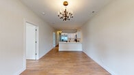 Located at 441 W Main St in Cary, IL, this thoughtfully designed single-floor home offers three bedrooms and two bathrooms within a well-proportioned layout. The open-concept living and kitchen area serves as the heart of the home, anchored by a striking multi-arm chandelier and warm wood-look flooring that extends throughout. A bold dark wood front door with sidelights and transom window floods the entryway with natural light, creating a welcoming first impression. The kitchen features white shaker cabinetry, a peninsula with a double sink and matte black faucet, stainless steel appliances including a gas range, microwave, and dishwasher, and clean white countertops — all flowing seamlessly into the living area. The spacious primary bedroom includes a walk-in closet and is complemented by a en-suite bathroom showcasing floor-to-ceiling marble-look tile, a walk-in shower with a wood-tiled floor, a built-in niche, and a matte black fixtures. The second bathroom features the same elegant marble-look tile surrounding a soaking tub. Additional bedrooms offer natural light through large windows. The consistent use of warm flooring, neutral tones, and designer light fixtures throughout lends the home a cohesive, modern aesthetic.