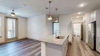 This well-appointed single-floor residence showcases a thoughtfully designed open-concept layout that seamlessly connects the kitchen and living areas. The kitchen is a standout feature, centered around a granite-topped island with an undermount sink and stylish industrial-style pendant lighting. Gray shaker-style cabinetry lines the walls, complemented by a stainless steel appliance suite including a refrigerator, microwave, and range, along with a classic white tile backsplash. Wood-look flooring runs throughout the main living areas, lending a warm, cohesive feel to the space.

The living area is bright and open, benefiting from a ceiling fan and a glass door that invites natural light while offering outdoor access. The bedroom features plush carpeting, dual windows with horizontal blinds, and a ceiling fan, creating a comfortable and restful retreat with views of the surrounding community.

The bathroom is finished to a high standard, featuring a granite-topped vanity with gray cabinetry, a walk-in glass-enclosed shower, and wood-look flooring that ties back to the rest of the unit. A dedicated in-unit laundry closet with full-size washer and dryer adds a practical and convenient touch to this move-in-ready residence.