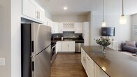 This single-floor residence offers a thoughtfully designed layout that balances comfort and functionality throughout its key living spaces. The open-concept floor plan seamlessly connects the kitchen and living area, creating an inviting atmosphere ideal for both daily living and entertaining.

The kitchen is a standout feature, showcasing crisp white shaker-style cabinetry, dark countertops, and a gray tile backsplash. A full suite of stainless steel appliances — including a refrigerator, range, microwave, and dishwasher — complements the space, while a built-in wine rack cabinet adds a distinctive touch. A kitchen island with matching dark countertop provides additional prep and dining space, and warm wood-tone flooring ties the area together.

The living room is bright and welcoming, with multiple windows dressed in white blinds that allow generous natural light to fill the room. Wood-look flooring continues throughout, adding warmth and visual continuity.

The bedroom is a calm retreat, featuring a ceiling fan, a built-in closet with shelving, and neutral gray walls that create a restful ambiance. Carpeted flooring adds comfort underfoot.

The bathroom is finished with elegant marble-patterned tile lining the tub and shower surround, complemented by sliding glass doors and brushed nickel fixtures, offering a clean and polished aesthetic.