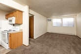 Located at 6316 Urbandale Ave in Des Moines, Iowa, this 2-bedroom, 1-bathroom unit offers a straightforward and functional single-floor layout. The space includes a living room, two bedrooms, a galley-style kitchen, a full bathroom, and a connecting hallway. Throughout the unit, neutral-toned carpet covers the floors, complemented by clean white walls and textured ceilings that give each room a consistent, understated aesthetic. Both bedrooms are modestly sized, each featuring a window with blinds that allows natural light to filter in, along with baseboard heating units to maintain warmth. The primary bedroom also includes a wall-mounted air conditioning unit. The galley kitchen is efficiently arranged with warm oak cabinetry lining both walls, light countertops, tile-style flooring, and white appliances including a range, microwave, dishwasher, and refrigerator — maximizing utility within a compact footprint. The bathroom is clean and simple, equipped with a full soaking tub and shower combo featuring built-in shelving, alongside standard fixtures. A hallway connects the main living areas to the bedrooms and bathroom, with wood-toned doors throughout adding a touch of warmth to the interior. A ceiling fan is also present, contributing to overall climate comfort.