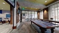 Located at 3111 S St in Sacramento, CA, this single-floor fitness and recreation facility offers a comprehensive wellness experience across a generously sized footprint. The space is divided into two well-appointed exercise rooms and a multipurpose lounge area, each thoughtfully designed with a contemporary aesthetic featuring yellow-green accent ceilings, dark trim, and modern finishes throughout.

The main fitness floor is expansive and bathed in natural light through large floor-to-ceiling windows that overlook an outdoor pool area with palm trees. This room is fully equipped with a wide array of cardio machines—including treadmills, ellipticals, stair climbers, and stationary bikes—alongside a dedicated strength training section featuring cable machines, free weights, benches, and resistance equipment. Motivational fitness photography adorns the walls, and ceiling fans and pendant lighting enhance the open, energetic atmosphere.

A secondary studio room features wood-plank flooring, TRX suspension trainers, spin bikes, yoga mats, and a large display screen ideal for guided workouts and group classes. Mirror walls amplify the sense of space in this versatile room.

The recreation lounge completes the facility, offering a full-size billiard table and shuffleboard set against patterned carpet, warm wood wall panels, frosted glass partitions, and sheer curtain-draped windows—creating a sophisticated, social atmosphere.