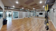 Located at 1335 West Summit Parkway in Spokane, WA, this fitness facility offers a comprehensive, single-floor layout designed to support a wide range of workout modalities. The space is divided into several distinct functional zones, each thoughtfully outfitted for its purpose.

The centerpiece of the facility is a spacious dance and movement studio featuring warm hardwood flooring, full-length mirrored walls, and acoustic panels mounted to the ceiling for sound management. Recessed lighting and an exposed HVAC duct system contribute to the room's clean, functional aesthetic. A mounted flat-screen display and an adjoining windowed room add versatility to the studio.

The main gym floor features polished concrete flooring and an open, industrial feel with exposed ceiling joists and truss work overhead. This area houses a robust selection of strength training equipment, including a cable machine, a full dumbbell rack, kettlebells, medicine balls, resistance tools, and a rowing machine. Rubber flooring mats define dedicated workout zones throughout the space.

A cardio section along the perimeter offers treadmills and elliptical machines positioned beside large windows that bring in natural light and views of the surrounding area. An additional room visible from the main floor appears to serve as a suspension training or functional fitness space. The facility is well-ventilated throughout, with ductwork and climate systems visible across all zones.
