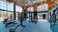 This two-floor fitness facility combines industrial architecture with a comprehensive suite of workout spaces. Exposed brick walls, soaring ceilings with visible ductwork, and floor-to-ceiling windows define the main weight training floor, flooding the space with natural light and offering views of the surrounding urban streetscape. The strength training area features multiple power racks, barbells, plate-loaded stations, and a full dumbbell rack arranged across resilient blue rubber flooring, all framed by bold athletic murals that energize the environment.

A dedicated cardio zone houses rows of treadmills, elliptical trainers, and stair climbers positioned along large windows, maximizing natural light during workouts. Warm hardwood flooring transitions the space from high-intensity zones into more functional training areas, including a room equipped with rowing machines and a dramatic black-and-white fitness mural. A versatile studio space features hardwood floors, large wall mirrors, spin bikes, and stability balls, making it well-suited for cycling classes and group training. An additional movement room boasts a vibrant, colorfully painted brick mural and clean hardwood flooring, ideal for yoga and stretching. Throughout both floors, pendant lighting, motivational artwork, and a cohesive dark and teal color palette create a focused and dynamic training environment.