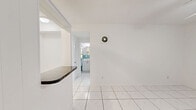Located at 5791 SW 74th Terr in South Miami, FL, this single-floor, one-bedroom, one-bathroom unit offers a efficiently designed layout surrounded by lush tropical greenery. The interior features consistent large-format white ceramic tile flooring throughout, lending a clean, cohesive look to the space.

The living area is bright and open, finished in crisp white walls with a wall-mounted ventilation unit and ample room for furnishings. A ceiling fan provides additional airflow, complementing the warm South Florida climate.

The bedroom is a comfortable, well-proportioned space highlighted by a ceiling fan with integrated lighting, generous built-in closet storage along one wall, and white-painted cabinetry. A window with blinds allows for natural light and ventilation.

The bathroom is a standout feature, showcasing retro-style teal and white vertically striped wall tiles surrounding a full bathtub and shower combination. A window above the toilet brings in natural light, enhancing the vibrant, vintage character of the room.

An aerial view of the property reveals a verdant setting with mature tropical trees framing the structure, adding privacy and a distinctive South Miami ambiance to this straightforward and functional unit.
