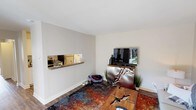 This single-floor residence offers a thoughtfully arranged layout with distinct living, dining, sleeping, and kitchen areas. The living room serves as a central gathering space, featuring warm wood-look flooring, a vibrant multicolored area rug, and an eye-catching wall-mounted pass-through shelf connecting to the kitchen. A metallic entertainment console anchors one wall, while a natural wood slab coffee table and neutral sofa add an eclectic, artistic character reinforced by bold abstract wall art.

The kitchen is outfitted with white shaker-style cabinetry, rich granite-look countertops, a classic white subway tile backsplash, and stainless steel appliances. A separate dining area features carpeted flooring and accommodates a round table, complemented by a mid-century credenza and vibrant artwork.

The bedroom is carpeted and generously sized, with large windows fitted with wide-slat blinds that allow ample natural light. A walk-in closet provides practical storage. Two full bathrooms each include a tub and shower combination, white vanities with single-basin sinks, large mirrors, and neutral wall tones, offering clean, functional spaces throughout.
