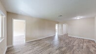 This single-story home offers a clean, open layout finished consistently with wood-look luxury vinyl plank flooring throughout. The interior is defined by warm neutral tones on the walls, crisp white baseboards, and textured ceilings that complement the overall light and airy atmosphere.

The spacious living area serves as the heart of the home, featuring a front-facing window that draws in natural light and connects the space to the outdoors. Multiple interconnected rooms extend from this central area, each maintaining the same cohesive flooring and color palette.

The kitchen is outfitted with white shaker-style cabinetry, granite countertops with subtle speckled detailing, a stainless steel sink, and a white range with overhead ventilation. The layout is efficient and functional, with ample counter and storage space.

Additional rooms throughout the home are well-proportioned and bathed in natural light from large windows that frame views of surrounding greenery. One room features a walk-in closet area with wire shelving, paired with a vanity showcasing matching granite countertops and a white cabinet base — indicating a primary suite setup.

The floor plan flows logically from room to room, offering a well-connected and practical single-level living experience with consistent, modern finishes throughout.