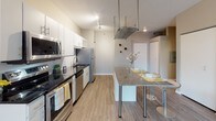 Located at 1367 Willow St in Minneapolis, MN, this single-floor residence offers a thoughtfully designed layout that balances comfort and modern style. The open-concept living area features wood-style flooring, large windows that invite generous natural light, and a neutral color palette that creates a calm, welcoming ambiance. The kitchen is well-equipped with stainless steel appliances, white cabinetry, a dark granite countertop island with bar seating, and track lighting overhead — making it both functional and visually appealing. An adjacent view reveals an additional kitchen configuration with dark countertops, white cabinets, and a stainless steel refrigerator, reflecting a practical and clean design. The bedroom is carpeted for comfort and features large windows with blinds, offering a restful retreat. The full bathroom is finished in crisp white tones with wood-style flooring, a single vanity with ample counter space, and a tub-shower combination. A standout feature is the stacked in-unit washer and dryer conveniently located within the bathroom. Throughout the space, consistent neutral wall tones and modern fixtures contribute to a cohesive and contemporary living environment.