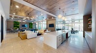 This thoughtfully designed single-floor amenity clubhouse combines contemporary style with versatile functionality across a generous, open layout. The central gathering area features a large kitchen island with quartz countertops and wood-tone cabinetry, anchored by elegant globe pendant lighting and a striking wood-paneled ceiling. The open-plan social lounge flows seamlessly from the kitchen, offering comfortable seating arrangements, a wall-mounted display, and a vibrant living moss wall accent that adds a natural, refreshing element to the interior.

Adjacent to the lounge, a games area houses a full-size billiards table beneath sculptural sputnik chandeliers, with additional seating and curated artwork lining the walls. A dining nook bathed in natural light from floor-to-ceiling black-framed windows provides direct views of an outdoor pool and courtyard area.

The business and co-working wing features private conference rooms enclosed by glass partition walls with black steel framing, a dedicated workspace corridor with built-in desks, and a compact kitchenette with sleek white cabinetry. Smaller private meeting pods with wall-mounted screens offer intimate spaces for focused work or calls. Throughout, light wood-look tile flooring, neutral tones, and carefully selected artwork create a polished, welcoming atmosphere.