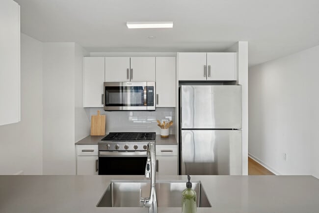 Renovated Package I kitchen with stainless steel appliances, white cabinetry, tile backsplash, grey quartz countertops, and hard-surface flooring - Avalon Riverview