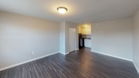 This single-floor unit offers a straightforward, functional layout with consistent dark hardwood-style flooring running throughout the main living areas, providing a cohesive and clean aesthetic. The living space is open and adequately sized, featuring neutral-toned walls, white baseboards, and a textured ceiling with flush-mount lighting that brightens the interior. A window unit air conditioner is installed in one room alongside a window fitted with blinds, allowing for natural light and ventilation. A solid entry door with a deadbolt provides secure access to the unit.

The kitchen is positioned toward the rear of the living area and is equipped with white upper cabinetry, a black refrigerator, a dishwasher, and a sink beneath upper cabinets — offering efficient use of the available space. A closet adjacent to the kitchen entry provides additional storage.

The bathroom includes a full tub-shower combo with built-in shelving, a toilet, and a vanity sink topped with a granite-style countertop. Textured walls and a mirror complete the space. Overall, the unit presents a clean, no-frills interior suited for practical, everyday living.