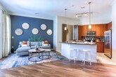 Located in Brookhaven, Georgia, this single-floor residence offers a thoughtfully designed open-concept layout that seamlessly connects the kitchen, dining, and living areas. The gourmet kitchen is a standout feature, showcasing rich walnut-toned cabinetry, granite countertops with a mosaic tile backsplash, stainless steel appliances, and a breakfast bar with pendant lighting — ideal for both cooking and casual dining. Adjacent to the kitchen, the dedicated dining area accommodates a round glass-top table and benefits from a clean, neutral palette that keeps the space feeling bright and airy. The living room is anchored by warm hardwood-style flooring, crown molding, and a dramatic dark accent wall. Floor-to-ceiling windows flood the space with natural light and provide views of the outdoor surroundings, including access to an outdoor area via a glass door. The bedroom is a serene retreat with plush carpeting, large windows overlooking the community pool, and soft, neutral tones. The bathroom features a full soaking tub with subway tile surround, granite vanity, and wood-toned cabinetry, maintaining the residence's cohesive modern aesthetic throughout.
