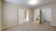 Located at 501 Phillips Ln in Statesville, NC, this single-floor residence offers a practical and well-organized layout across two bedrooms and two full bathrooms. The combined kitchen and living area forms the heart of the home, featuring an open peninsula that separates the kitchen from the carpeted living space. The kitchen is equipped with ample white cabinetry, dark countertops, a range, a dishwasher, and a refrigerator, complemented by a pendant light over the peninsula. The spacious living room benefits from natural light through windows fitted with blinds and includes a private exterior door providing outdoor access. The primary bedroom is generously sized, featuring plush carpeting, a dedicated closet, and a connected en-suite bathroom. The second bedroom also offers carpeting and a window with natural light. Both bathrooms include a tub-shower combination, a vanity with dark countertops, and wood-look flooring. A dedicated laundry room provides washer and dryer hookups along with a wire shelving unit for added storage. Throughout the residence, neutral warm-beige walls and textured ceilings contribute to a consistent and understated aesthetic.