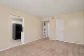 This single-story unit offers a practical and comfortable layout across two bedrooms, one bathroom, a kitchen, and a dedicated closet. The open living area is finished with soft wall-to-wall carpeting and neutral walls that create a warm, welcoming atmosphere. A large window allows natural light to fill the space, enhancing the bright and airy feel. The living area flows into the secondary bedroom, also carpeted and featuring a ceiling fan and its own window overlooking the outdoors.

The kitchen is outfitted with crisp white cabinetry, granite-style countertops, and tile flooring. It includes a full suite of appliances such as a range and refrigerator, along with ample counter and storage space arranged in an efficient layout.

The spacious primary bedroom includes a ceiling fan, access to a walk-in closet with built-in shelving and hanging rods, and a direct connection to the full bathroom. The bathroom features a tub-shower combination with tile surround, a toilet, vanity with a single sink, and tile flooring.

Throughout the unit, a consistent neutral color palette and textured ceilings contribute to a cohesive and tidy aesthetic, making this a well-organized and livable space.