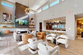 Located at 277 Clifton St SE in Atlanta, GA, this thoughtfully designed single-floor communal space delivers a seamless blend of modern aesthetics and functional comfort across a generously proportioned open-concept layout.

The living area commands immediate attention with its dramatic soaring ceilings and a bank of clerestory windows that flood the space with natural light. A striking floor-to-ceiling slatted wood feature wall anchors a marble-surround fireplace and mounted TV, flanked by floating shelves. Statement sputnik chandeliers add sculptural flair overhead, while light-toned hardwood flooring unifies the entire space.

Plush white boucle lounge chairs and warm cognac-toned seating arrangements provide ample, stylish gathering space. Full-height glass doors open directly to an outdoor pool area, enhancing the indoor-outdoor connection.

The kitchen features dark espresso cabinetry, sleek white quartz countertops, stainless steel appliances, and a long bar-height island illuminated by a row of matte black pendant lights. Adjacent to the kitchen, the dining area offers a central table with upholstered chairs alongside cozy booth-style seating in gold and grey tones, with a wall-mounted counter and bar stools beneath a trio of windows — ideal for individual use or small group gatherings.