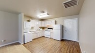 This 1-bedroom, 1-bathroom single-floor unit offers a practical and comfortable layout designed for efficient living. The kitchen is a functional highlight of the space, featuring white cabinetry, a full suite of white appliances including a refrigerator and electric range, a double-basin sink, and wood-look vinyl flooring. A stacked washer and dryer unit is conveniently integrated directly into the kitchen area, adding exceptional in-unit utility. The kitchen flows naturally into the entry and dining areas, which share the same durable wood-look flooring and are bathed in neutral, warm-toned walls throughout.

The living room is generously sized with soft carpeting underfoot and benefits from natural light through multiple windows fitted with blinds, as well as a glass-paneled exterior door that further brightens the space. The bedroom offers a comfortable footprint with plush carpeting, a window with blinds providing natural light, and access to a dedicated closet equipped with wire shelving for organized storage.

The bathroom features wood-look vinyl flooring consistent with the rest of the unit, a vanity with countertop sink, a toilet, and grab bars, suggesting accessibility-conscious design. Clean white trim and beige-toned walls provide a cohesive, neutral aesthetic throughout the entire space.