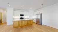 Located at 1545 Payne St in Tallahassee, FL, this well-appointed two-story home offers 3 bedrooms and 4 bathrooms thoughtfully distributed across two floors. The main level features a bright, open-concept living, dining, and kitchen area bathed in natural light from large windows and a glass-panel front door. Light hardwood floors flow seamlessly throughout, complementing the home's clean, modern aesthetic defined by crisp white walls and recessed lighting.

The kitchen is a standout feature, showcasing white shaker-style cabinetry extending to the ceiling, granite countertops, stainless steel appliances including a French door refrigerator and range, and a generous island with warm natural wood paneling — a striking design contrast. A dedicated pantry adds practical storage. Bathrooms are finished with granite-topped vanities and clean white fixtures, including tub-shower combinations.

The spacious primary bedroom upstairs includes a ceiling fan and access to a generously sized walk-in closet with built-in double hanging rods. With six closets total throughout the home, storage is abundant. A dedicated laundry area and an attached garage with automatic opener round out the functional amenities. The home's consistent use of light tones, quality finishes, and thoughtful layout create a bright, welcoming atmosphere throughout.