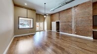 Located on Broad Street in Kingsport, Tennessee, this 3-bedroom, 2-bathroom residence offers a compelling mix of historic industrial character and contemporary upgrades. The open-plan living, dining, and kitchen area anchors the home, featuring soaring ceilings, exposed ductwork, and dramatic exposed brick walls that speak to the building's heritage. Large windows and a patio entry allow natural light to fill the expansive main area, complemented by warm hardwood-style flooring throughout. The kitchen is well-appointed with rich dark-espresso cabinetry, granite countertops, and a full suite of stainless steel appliances including a range, microwave, dishwasher, and refrigerator. The bedrooms continue the industrial aesthetic, with select rooms showcasing exposed brick accent walls alongside ceiling fans and generous closet space — the home features an impressive eight closets in total. The two bathrooms maintain a cohesive design with dark vanity cabinetry, granite countertops, and hardwood-style tile flooring, one bathroom highlighting an exposed brick wall for added character. A dedicated laundry room and a hallway connecting the private quarters complete the thoughtfully laid-out floor plan, making this a distinctive and functional home.