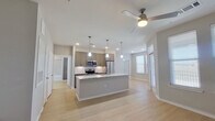 This thoughtfully designed single-floor residence offers a cohesive open-concept layout that maximizes functionality and visual flow throughout. The combined kitchen and living area serves as the heart of the home, anchored by a striking center island topped with granite countertops and illuminated by stylish pendant lighting. The kitchen is outfitted with stainless steel appliances, including a refrigerator, stove, and microwave, complemented by taupe cabinetry and a classic tile backsplash. Light hardwood-style flooring extends throughout the main living areas, while recessed lighting and a ceiling fan contribute to a bright and comfortable atmosphere. Multiple windows invite generous natural light into both the living space and the bedroom. The bedroom features plush carpet flooring, a ceiling fan, and ample natural light from dual windows, with access to a dedicated closet. A standout feature of this residence is the built-in entryway organizer, complete with hooks and open cubbies, offering convenient storage near the entry. The full bathroom is finished with a granite-topped vanity with gray cabinetry, a tiled tub-shower combination, and a tall storage cabinet, maintaining the cohesive modern aesthetic found throughout the home.