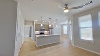 This thoughtfully designed single-floor residence offers a cohesive open-concept layout that maximizes functionality and visual flow throughout. The combined kitchen and living area serves as the heart of the home, anchored by a striking center island topped with granite countertops and illuminated by stylish pendant lighting. The kitchen is outfitted with stainless steel appliances, including a refrigerator, stove, and microwave, complemented by taupe cabinetry and a classic tile backsplash. Light hardwood-style flooring extends throughout the main living areas, while recessed lighting and a ceiling fan contribute to a bright and comfortable atmosphere. Multiple windows invite generous natural light into both the living space and the bedroom. The bedroom features plush carpet flooring, a ceiling fan, and ample natural light from dual windows, with access to a dedicated closet. A standout feature of this residence is the built-in entryway organizer, complete with hooks and open cubbies, offering convenient storage near the entry. The full bathroom is finished with a granite-topped vanity with gray cabinetry, a tiled tub-shower combination, and a tall storage cabinet, maintaining the cohesive modern aesthetic found throughout the home.