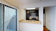 This single-floor space showcases a thoughtfully designed kitchen that serves as a focal point of the layout. The kitchen features dark espresso-toned cabinetry extending from floor to ceiling, providing generous storage while creating a bold visual contrast against the white walls. A granite peninsula countertop with warm, neutral tones doubles as a breakfast bar, offering both additional workspace and a casual dining option. The stainless steel appliances, including an electric range and over-the-range microwave, lend a contemporary, polished feel to the space. A stainless steel undermount sink is integrated into the peninsula, adding functionality to the open layout. Recessed flush lighting illuminates the kitchen area effectively. Adjacent to the kitchen, large floor-to-ceiling sliding glass doors flood the space with abundant natural light, enhancing the open and airy atmosphere. The white walls and ceilings throughout contribute to a clean, modern aesthetic that complements the darker kitchen elements, resulting in a well-balanced and visually appealing interior.