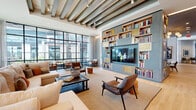 Located at 30 Peabody St in the heart of Nashville, TN, this expansive single-floor amenity space offers a richly designed environment that blends contemporary style with curated comfort. The layout encompasses multiple distinct zones across a generous footprint, each thoughtfully appointed to encourage both socializing and relaxation.

A standout lounge area features exposed beam ceilings, floor-to-ceiling steel-framed windows that flood the space with natural light, and a dramatic built-in bookcase wall with integrated shelving and a large flat-screen display. Plush seating arrangements invite conversation in an atmosphere that feels both refined and welcoming.

Additional gathering spaces showcase velvet lounge chairs, tufted banquette seating, and warm wood-slat ceiling accents, all set against a backdrop of carefully selected artwork and framed photography that pays homage to Nashville's cultural heritage. A dedicated billiards room with polished concrete floors and a wood-slatted ceiling provides a more casual, recreation-oriented retreat.

Light-filled transition corridors with light wood flooring, white brick accent walls, and sculptural pendant lighting connect the zones seamlessly. A kitchenette bar area and coffee station add functional convenience. Throughout, floor-to-ceiling windows frame views of the surrounding Nashville skyline, reinforcing the urban sophistication that defines this remarkable space.