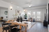 This thoughtfully designed single-floor residence offers 1 bedroom, 2 bathrooms, a dedicated office, and in-unit laundry across a well-proportioned open layout. Light-toned hardwood-style flooring runs throughout the main living areas, lending a clean, contemporary feel.

The kitchen serves as the centerpiece of the open-concept main area, featuring a large waterfall-edge quartz island with a single-basin sink and bar seating for casual dining. Flat-front taupe cabinetry reaches toward the ceiling, complemented by stainless steel appliances and recessed lighting accented by a statement brass pendant light. The kitchen flows directly into the living and dining areas, the latter of which connects to an outdoor balcony through a glass sliding door, filling the space with natural light.

The primary bedroom is generously sized with plush carpeting, a ceiling fan, and windows offering exterior views. The primary bathroom is long and well-appointed, featuring a dual-sink vanity with white countertops, wood-toned cabinetry, and a glass-enclosed walk-in shower. The second bathroom includes a single vanity and a shower with a curtain enclosure. The dedicated office features paneled wall detailing and a ceiling pendant, creating a polished, focused workspace. The in-unit laundry room houses a stacked washer and dryer for added convenience.