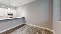 Located at 1230 Elm St in Manchester, NH, this 2-bedroom, 1-bathroom unit offers a thoughtfully designed single-floor layout with contemporary finishes throughout. The open-concept kitchen and dining area serves as the heart of the home, featuring white shaker-style cabinetry with matte black hardware, quartz countertops, a center island with an undermount sink, and a full suite of stainless steel appliances including a refrigerator, range, and over-the-range microwave. Pendant lighting above the island adds a modern touch, while wood-look luxury vinyl plank flooring ties the living and kitchen spaces together seamlessly. Both bedrooms are carpeted with a patterned, neutral-toned carpet and are finished with clean white walls and white panel doors, offering a calm and functional retreat. A transom window detail in the bedroom area allows for light transfer between spaces. The bathroom area includes in-unit stacked washer and dryer with additional cabinet storage for added convenience. The unit maintains a consistent, neutral gray and white color palette throughout, contributing to a clean, modern aesthetic that is both practical and inviting.
