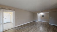 Located along Clark Road in Sarasota, Florida, this single-floor residence offers a well-designed layout with a clean, modern aesthetic throughout. The living areas are finished with durable wood-style flooring in warm, neutral tones, complemented by soft beige walls and crisp white baseboards that create a bright and cohesive atmosphere.

The open living and dining areas are generously proportioned, with the dining space anchored by an elegant multi-arm chandelier and a window fitted with vertical blinds that allows natural light to filter in. Sliding glass doors in the living area lead directly to an outdoor patio, bringing in additional light and providing easy access to exterior views.

The galley-style kitchen is efficiently arranged, featuring white cabinetry with brushed hardware, granite-patterned countertops, a stainless steel sink, and white appliances including a refrigerator, range, and built-in microwave — all designed to maximize function within a compact footprint.

The bedroom offers a calm, comfortable retreat with light wood-style flooring and a window dressed with vertical blinds overlooking greenery outside. The bathroom is neatly appointed with a white vanity, granite countertop, undermount sink, and matching brushed hardware, maintaining the consistent design language found throughout the unit.