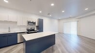 This well-designed one-bedroom, one-bathroom unit in West Valley City, Utah offers a thoughtfully laid-out single-floor plan with modern finishes throughout. The open-concept kitchen and living area serves as the heart of the home, highlighted by a striking two-tone cabinetry design featuring navy blue lower cabinets paired with crisp white upper cabinets. A large central island with a white quartz countertop provides additional prep and seating space, while a full suite of stainless steel appliances — including a refrigerator, range, microwave, and dishwasher — completes the kitchen. Light wood-look vinyl plank flooring flows seamlessly through the main living areas, complementing the clean white walls and recessed lighting overhead. The living room benefits from a sliding glass door with vertical blinds, allowing generous natural light to fill the space. The bedroom offers plush carpeting, a window with exterior views, and a dedicated closet. The bathroom features navy blue vanity cabinetry with a white countertop, a tub-shower combination, and consistent modern hardware throughout. Clean lines, neutral tones, and contemporary design choices give this unit a bright, cohesive, and functional aesthetic.