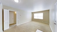 This single-floor space presents a clean, functional layout with a straightforward and comfortable design. The main room is finished with wall-to-wall beige carpeting that adds warmth underfoot, while the walls are painted in a soft, neutral tan tone that creates a calm and inviting ambiance throughout.

A large, centrally positioned window along the far wall allows natural light to fill the room, brightening the space and offering an airy feel. White baseboards provide a crisp contrast against the neutral walls and flooring, contributing to the room's tidy, well-maintained appearance.

A doorway off to one side leads to an adjacent area, accompanied by a closet featuring classic louvered bi-fold doors — a practical storage solution that blends seamlessly with the overall aesthetic. The ceiling is smooth and white, fitted with a flush-mount light fixture that ensures even illumination throughout the room.

Overall, this space offers a neutral, move-in-ready environment with understated finishes that provide a versatile backdrop suitable for a variety of uses and personal styles.