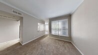 This single-floor residence offers a thoughtfully designed layout that balances comfort and functionality throughout. The living area is generously proportioned, featuring plush wall-to-wall carpeting, neutral taupe walls, and elegant crown molding that adds a refined architectural detail. A large window fitted with white horizontal blinds allows natural light to fill the space while providing views of lush greenery outside.

The kitchen is well-equipped with white cabinetry, light wood-look vinyl plank flooring, laminate countertops, a stainless steel sink, and a full suite of black appliances including a range, microwave, dishwasher, and refrigerator. The galley-style layout maximizes efficiency and storage.

The bedrooms are carpeted and bright, each featuring windows with blinds that invite natural light. One bedroom includes a built-in desk with shelving and drawers — a practical feature ideal for a home office setup — along with access to a hallway with closets. Another bedroom is equipped with a ceiling fan and direct access to an adjacent room.

The bathroom is clean and functional, featuring a tub-shower combination with tiled surround, a vanity with a vessel-style sink, and updated brushed nickel fixtures. A dedicated laundry area with washer and dryer hookups is conveniently accessible nearby. Throughout, the space maintains a cohesive, neutral aesthetic suited for a variety of living arrangements.