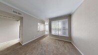 This single-floor residence offers a thoughtfully designed layout that balances comfort and functionality throughout. The living area is generously proportioned, featuring plush wall-to-wall carpeting, neutral taupe walls, and elegant crown molding that adds a refined architectural detail. A large window fitted with white horizontal blinds allows natural light to fill the space while providing views of lush greenery outside.

The kitchen is well-equipped with white cabinetry, light wood-look vinyl plank flooring, laminate countertops, a stainless steel sink, and a full suite of black appliances including a range, microwave, dishwasher, and refrigerator. The galley-style layout maximizes efficiency and storage.

The bedrooms are carpeted and bright, each featuring windows with blinds that invite natural light. One bedroom includes a built-in desk with shelving and drawers — a practical feature ideal for a home office setup — along with access to a hallway with closets. Another bedroom is equipped with a ceiling fan and direct access to an adjacent room.

The bathroom is clean and functional, featuring a tub-shower combination with tiled surround, a vanity with a vessel-style sink, and updated brushed nickel fixtures. A dedicated laundry area with washer and dryer hookups is conveniently accessible nearby. Throughout, the space maintains a cohesive, neutral aesthetic suited for a variety of living arrangements.