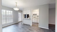 Located at 8623 Starcrest Dr in San Antonio, TX, this 2-bedroom, 1-bathroom single-floor unit offers a practical and well-organized layout. Wood-look vinyl plank flooring runs consistently throughout all rooms, complemented by light gray walls and clean white trim, creating a cohesive and neutral aesthetic.

The kitchen is a galley-style space featuring white cabinetry, black appliances including a gas range, dishwasher, and refrigerator, along with a double sink. A pass-through counter opens directly to the living area, enhancing the sense of openness between the two spaces. The living room benefits from natural light provided by large windows fitted with horizontal blinds.

Both bedrooms include ceiling fans with light fixtures and windows that bring in natural light and outdoor views. The primary bedroom offers a generous footprint and features a double-door closet, providing ample storage. The second bedroom also includes closet access via a single door.

The bathroom is outfitted with a full tub-shower combination with white tile surround, a vanity with a speckled countertop, and wood-look flooring consistent with the rest of the unit. A hallway connects the main living areas to the bedrooms and bathroom. Textured ceilings are present throughout the unit.