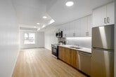 Located at 99 Milford Ave in Waterloo, Ontario, this two-bedroom, one-bathroom unit offers a thoughtfully designed single-floor layout with a clean, contemporary aesthetic. Light-toned hardwood-style flooring runs continuously throughout the space, complementing crisp white walls and creating a bright, cohesive atmosphere.

The open living area connects directly to a compact, well-appointed kitchen featuring warm wood-toned cabinetry, white upper cabinets, stainless steel appliances including an electric range, microwave, and refrigerator, and a simple countertop with an undermount sink. Recessed pot lighting illuminates the main living and kitchen area efficiently.

A hallway leads to the two bedrooms and bathroom. The generously sized primary bedroom occupies a substantial portion of the unit's total footprint, offering ample space for furnishings. Both bedrooms feature the same light flooring and neutral walls, with one bedroom including a sliding double-door closet and another benefiting from a window with an outdoor view, allowing natural light to enter.

The bathroom is finished in a modern style, featuring a wood-grain vanity with a white countertop, undermount sink, chrome fixtures, and a large frameless mirror. Overall, the unit presents a clean, move-in-ready interior with consistent modern finishes throughout.