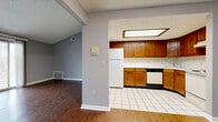 Located at 67 Oakridge Dr in Buffalo, NY, this single-floor unit offers a practical and well-organized layout with a neutral gray color palette throughout. The living area is generously sized, featuring rich dark hardwood-style flooring, vaulted ceilings that add a sense of openness, and a sliding glass door that brings in natural light and provides views of the surrounding neighborhood. An adjacent entry area also benefits from the vaulted ceiling detail, enhancing the spacious feel of the common areas. The kitchen is open to the main living space and is equipped with warm oak cabinetry, white countertops, white tile flooring, a white refrigerator, a white electric range, and a dishwasher. A pass-through window connects the kitchen to a secondary area, adding functional versatility. The bedrooms feature hardwood-style flooring and large windows that allow ample natural light to filter in, with views of the surrounding area. The bathroom includes a full tub-shower combination, a wood-cabinet vanity with a white countertop, and tile flooring. Throughout the unit, clean white baseboards and consistent gray walls contribute to a cohesive, move-in-ready aesthetic.