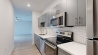 This single-story unit offers a thoughtfully designed layout across a compact yet efficient floor plan. The primary bedroom is notably generous in size, featuring light wood-style flooring, a ceiling fan with integrated lighting, and a large window fitted with horizontal blinds that allow natural light to filter throughout the space. The room provides direct access to the bathroom, creating a practical flow between spaces.

The galley-style kitchen is well-appointed with modern grey cabinetry featuring brushed nickel hardware, white quartz countertops, and a classic white subway tile backsplash. A full suite of stainless steel appliances includes an electric range, over-the-range microwave, dishwasher, and refrigerator. A stacked washer and dryer unit is also accommodated within the kitchen corridor, adding functional convenience.

The bathroom features a white vanity with a quartz countertop, an undermount sink with brushed nickel fixtures, and a large frameless mirror. Light wood-style flooring carries throughout the unit, maintaining a cohesive and clean aesthetic. Crisp white walls and recessed lighting contribute to an overall bright, contemporary ambiance throughout the space.