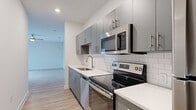This single-story unit offers a thoughtfully designed layout across a compact yet efficient floor plan. The primary bedroom is notably generous in size, featuring light wood-style flooring, a ceiling fan with integrated lighting, and a large window fitted with horizontal blinds that allow natural light to filter throughout the space. The room provides direct access to the bathroom, creating a practical flow between spaces.

The galley-style kitchen is well-appointed with modern grey cabinetry featuring brushed nickel hardware, white quartz countertops, and a classic white subway tile backsplash. A full suite of stainless steel appliances includes an electric range, over-the-range microwave, dishwasher, and refrigerator. A stacked washer and dryer unit is also accommodated within the kitchen corridor, adding functional convenience.

The bathroom features a white vanity with a quartz countertop, an undermount sink with brushed nickel fixtures, and a large frameless mirror. Light wood-style flooring carries throughout the unit, maintaining a cohesive and clean aesthetic. Crisp white walls and recessed lighting contribute to an overall bright, contemporary ambiance throughout the space.