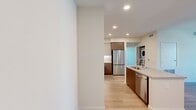 North Grove B2A is a thoughtfully designed 2-bedroom, 2-bathroom apartment spanning 870 square feet on a single floor in Riverside, CA 92501. The modern exterior features a contemporary multi-story building with clean stucco facades, large windows, and a well-maintained parking area. Inside, the open kitchen and living area serve as the heart of the unit. The kitchen is outfitted with stainless steel appliances including a range, over-the-range microwave, and refrigerator, complemented by two-tone cabinetry — white uppers and warm wood-grain lowers — a marble-style tile backsplash, quartz countertops, and a kitchen island with a sink. Light wood-style flooring runs through the living and dining areas, which feature large windows and a sliding glass door that bring in natural light and views of the community. The primary bedroom measures 130 square feet and includes plush carpeting, a dedicated closet, and en-suite access. The second bedroom is similarly carpeted and well-lit. Both bathrooms feature tub/shower combinations with clean white tile surrounds, brushed nickel fixtures, grab bars, and wood-look flooring. Additional features include two closets, a hallway, and accessible design elements throughout.