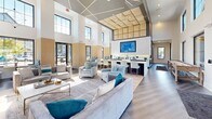 This expansive 2,140 square foot clubhouse at Prism At Dimond Ridge exemplifies modern architectural design with its open-concept layout and soaring ceilings. The space is bathed in natural light from large windows, creating an airy and inviting atmosphere. The interior showcases a harmonious blend of contemporary and comfortable elements, with a color palette dominated by neutrals accented with pops of blue and teal.

The main living area features plush seating arrangements, including a stylish sectional sofa and accent chairs, perfect for socializing or relaxation. A state-of-the-art entertainment system with a large flat-screen TV is seamlessly integrated into the decor. The space flows into a well-appointed kitchenette area, complete with sleek countertops and bar seating, ideal for casual dining or entertaining.

Additional amenities include a games area, possibly featuring a pool table, and various seating nooks for more intimate gatherings. The clubhouse's design incorporates modern lighting fixtures, including striking ceiling installations that add visual interest and warmth to the space. Thoughtful decorative touches, such as geometric wall art and mirrors, contribute to the overall sophisticated ambiance.

The flooring transitions from warm wood-look planks to plush area rugs, defining different functional zones within the open layout. Floor-to-ceiling glass doors lead to an outdoor patio area, extending the living space and providing seamless indoor-outdoor flow. This meticulously designed clubhouse offers residents a luxurious and versatile community space for a variety of activities and events.