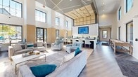 This expansive 2,140 square foot clubhouse at Prism At Dimond Ridge exemplifies modern architectural design with its open-concept layout and soaring ceilings. The space is bathed in natural light from large windows, creating an airy and inviting atmosphere. The interior showcases a harmonious blend of contemporary and comfortable elements, with a color palette dominated by neutrals accented with pops of blue and teal.

The main living area features plush seating arrangements, including a stylish sectional sofa and accent chairs, perfect for socializing or relaxation. A state-of-the-art entertainment system with a large flat-screen TV is seamlessly integrated into the decor. The space flows into a well-appointed kitchenette area, complete with sleek countertops and bar seating, ideal for casual dining or entertaining.

Additional amenities include a games area, possibly featuring a pool table, and various seating nooks for more intimate gatherings. The clubhouse's design incorporates modern lighting fixtures, including striking ceiling installations that add visual interest and warmth to the space. Thoughtful decorative touches, such as geometric wall art and mirrors, contribute to the overall sophisticated ambiance.

The flooring transitions from warm wood-look planks to plush area rugs, defining different functional zones within the open layout. Floor-to-ceiling glass doors lead to an outdoor patio area, extending the living space and providing seamless indoor-outdoor flow. This meticulously designed clubhouse offers residents a luxurious and versatile community space for a variety of activities and events.