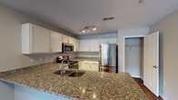 Located at 2425 Summerlin Ridge Rd in Winston-Salem, NC, this single-floor residence offers a well-designed layout with a cohesive, modern aesthetic throughout. The open-concept living area is anchored by rich, dark hardwood-style flooring that extends seamlessly through the main living spaces, complemented by neutral warm-gray walls and textured ceilings. The spacious living room receives natural light through a large window fitted with blinds and features a ceiling fan with light fixture overhead.

The kitchen is a functional highlight, equipped with white shaker-style cabinetry, granite countertops with warm tonal variation, and a full suite of stainless steel appliances including a refrigerator with bottom freezer, electric range, and over-the-range microwave. A peninsula with an undermount sink provides additional prep space and casual seating potential, with track lighting illuminating the workspace above.

The bedroom offers generous proportions, hardwood-style flooring, and direct access to a dedicated walk-in closet with built-in shelving and hanging rods. The bathroom includes a tub/shower combination, toilet, and vanity, all finished with consistent flooring and neutral tones. A dedicated laundry closet houses a full-size GE washer and dryer with overhead wire shelving for added storage convenience.