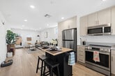 Located in Lancaster, CA, this well-appointed single-story home offers three bedrooms and two bathrooms across a thoughtfully designed floor plan. The open-concept kitchen and living area serves as the heart of the home, featuring crisp white cabinetry extending to the ceiling, stainless steel appliances including a range, microwave, and refrigerator, and a central island with a butcher block top and seating. Light wood-style flooring flows throughout, enhancing the clean, modern aesthetic. The living room is bright and welcoming, with recessed lighting, large windows that invite natural light, and a neutral color palette that complements any decor. The primary bedroom is a comfortable retreat with windows on multiple walls, filled with natural light, and accompanied by a dedicated walk-in closet featuring built-in shelving and hanging rods. The en-suite primary bathroom includes a white vanity and a separate water closet. A second full bathroom offers a tub-shower combination with white tile surround and built-in open shelving. Additional bedrooms are well-sized with ample natural light. Throughout the home, the consistent use of light tones, recessed lighting, and wood-look flooring creates a cohesive, airy ambiance ideal for modern living.