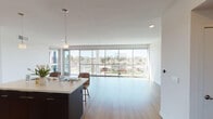 Located at 1000 Elements Way in Irvine, CA, this contemporary single-floor residence showcases a clean, modern design throughout. The open-concept living and dining area is defined by sweeping floor-to-ceiling glass walls that flood the space with abundant natural light and frame expansive views of the surrounding Irvine cityscape and lush tree-lined streetscapes. Light hardwood flooring extends through the main living areas, enhancing the bright, airy atmosphere.

The kitchen is thoughtfully designed with a striking contrast of dark cabinetry and crisp white upper cabinets, complemented by quartz countertops, a subway tile backsplash, and a full suite of stainless steel appliances including a gas range, built-in microwave, and side-by-side refrigerator. A central island with bar seating and pendant lighting serves as both a functional workspace and a casual gathering spot.

The bedrooms feature plush carpeting, ceiling fans, generous closet space, and large windows that invite natural light. The bathroom is well-appointed with a soaking tub and shower combination, a dark-cabinet vanity, and a large mirror. An in-unit stacked washer and dryer adds everyday convenience. The private balcony offers open-air views of the Irvine skyline, perfect for enjoying Southern California's temperate climate.