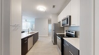 This well-designed single-floor unit offers four bedrooms and four full bathrooms, making it an ideal layout for shared or multi-occupant living. The open-concept kitchen and living area serves as the heart of the home, showcasing a sleek two-tone design with dark lower cabinetry contrasted by crisp white upper cabinets. A large kitchen island with a white quartz-style countertop doubles as a breakfast bar with seating, while a full suite of stainless steel appliances — including a refrigerator, range, built-in microwave, and dishwasher — completes the functional cooking space. Light wood-style flooring flows seamlessly throughout, enhancing the bright, airy feel created by the white walls and neutral palette. The living area offers natural light through slatted blinds and includes a ceiling fan for comfort. Each bedroom is a comfortable, private space with individual windows and easy access to one of the four bathrooms. The bathrooms feature clean white finishes, single-sink vanities with under-cabinet storage, lighted mirrors, and tub-shower combinations. Five closets are distributed throughout the unit, providing generous storage. The overall design is contemporary and functional, maintaining a consistent minimalist aesthetic.