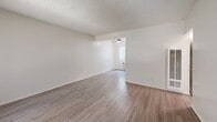 Located in Santa Ana, CA, this efficiently designed one-bedroom, one-bathroom residence offers a thoughtful layout across a single floor. The living room serves as the welcoming heart of the space, featuring wood-style laminate flooring, neutral white walls, a textured ceiling, and a large window fitted with vertical blinds that invites natural light and offers a view of the surrounding greenery. A ceiling fan adds comfort to the open feel of the room.

The kitchen is bright and functional, outfitted with white cabinetry, light granite-style countertops, a double-basin sink, a coil-top electric range, and a full-size refrigerator. Wood-style flooring continues throughout, and a window above the sink brings in additional natural light. A wall-mounted AC unit provides climate control.

The bedroom offers a carpeted floor, clean white walls, and a textured ceiling, providing a quiet and comfortable retreat. A hallway connects the main living areas to the bedroom and bathroom, supporting a practical flow throughout the unit.

The bathroom is clean and well-appointed, featuring a shower-tub combo, a toilet, and a vanity with granite-style countertop, white cabinetry, and a mirror. Wood-style flooring and a small window complete the space, maintaining the consistent, bright aesthetic found throughout the home.
