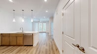 Located at 10001 Turkey Creek Rd in College Station, TX, this single-floor, one-bedroom, one-bathroom residence offers a well-designed layout that maximizes functionality and comfort. The open-concept kitchen and living area serves as the heart of the home, featuring warm hardwood-style flooring throughout. The kitchen is appointed with two-tone cabinetry — natural wood lower cabinets paired with white upper cabinets — complemented by a white subway tile backsplash, a large peninsula with pendant lighting, stainless steel appliances including a French door refrigerator and built-in microwave, and a deep undermount sink. The living area benefits from natural light via French doors that open to a private outdoor area, with a ceiling fan overhead. The bedroom continues the warm aesthetic with plush carpet, a ceiling fan, and a window overlooking greenery. It connects directly to a dedicated closet outfitted with dual hanging rods and shelving. The bathroom is elegantly finished with large-format tile flooring, an extended dual-sink vanity with ample cabinetry, stylish wall-mounted lighting, and a glass-enclosed walk-in shower with subway tile surround. Clean white walls and neutral tones throughout create a bright, cohesive atmosphere.