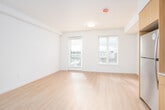 This well-designed single-floor unit offers a clean, modern aesthetic with light wood-style flooring that flows seamlessly throughout every room, creating a warm and cohesive feel. The open-concept layout connects the kitchen and living area, maximizing the sense of space and encouraging easy movement between functional zones.

The kitchen is a standout feature, outfitted with a full suite of stainless steel appliances including a refrigerator, electric range, over-the-range microwave, and dishwasher. Warm wood-toned cabinetry extends from floor to ceiling, offering generous storage, while white subway tile backsplash and light countertops add a crisp, contemporary contrast.

The living area is bright and open, benefiting from multiple windows that invite natural light and offer views of the surrounding neighborhood. A door provides direct outdoor access, further enhancing the airy ambiance of the space.

The bathroom is finished in a clean, minimal style, featuring a full soaking tub with shower, a vanity with a wood-accented cabinet, and a towel bar — all set against white walls and matching flooring.

Additional highlights include a spacious walk-in closet equipped with wire shelving and hanging rods, providing practical and well-organized storage. Recessed and flush-mount ceiling lighting is found throughout, ensuring consistent illumination across all areas of the unit.